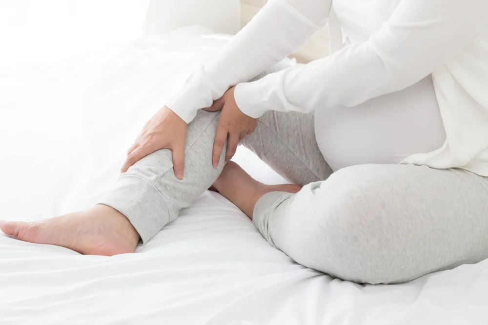 A pregnant woman in her third trimester massages her inner thigh leg.